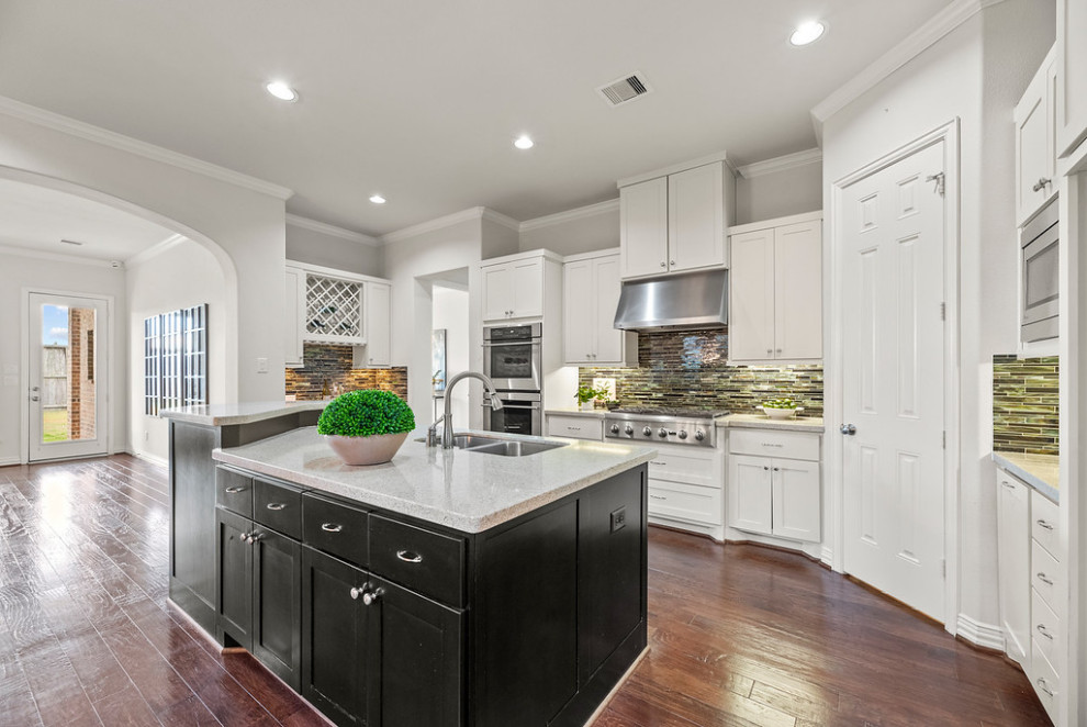 This is an example of a transitional kitchen in Houston with white cabinets, multi-coloured splashback, stainless steel appliances and with island.