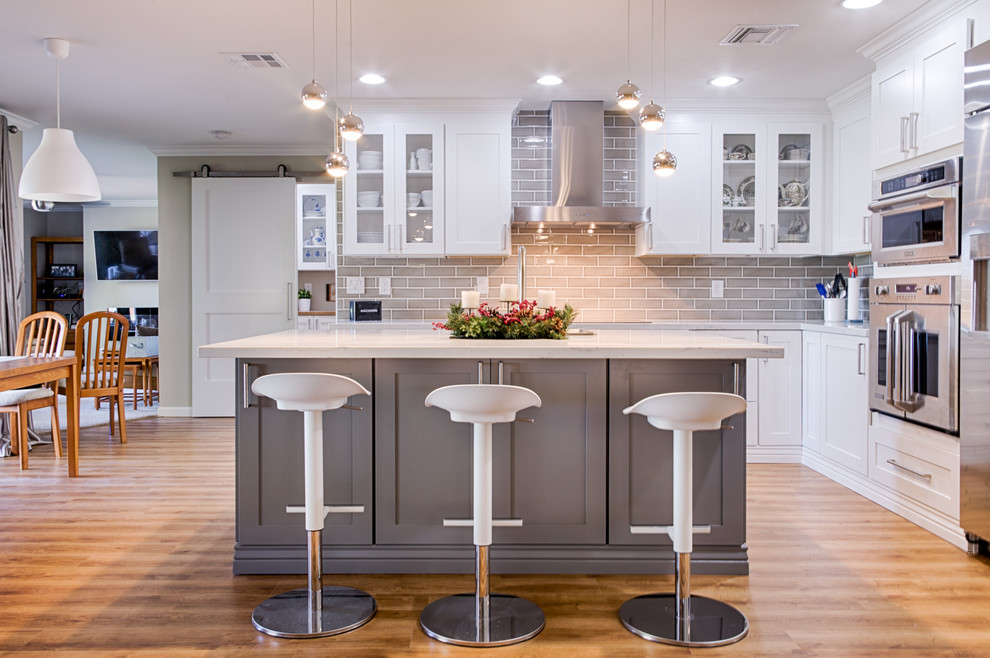 Inspiration for a mid-sized transitional l-shaped laminate floor open concept kitchen remodel in Phoenix with an undermount sink, shaker cabinets, white cabinets, quartzite countertops, gray backsplash, ceramic backsplash, stainless steel appliances and an island