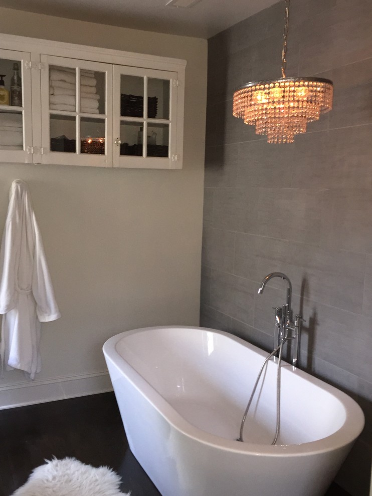 Inspiration for a small modern master bathroom in Raleigh with glass-front cabinets, white cabinets, a freestanding tub, gray tile, porcelain tile, white walls and dark hardwood floors.