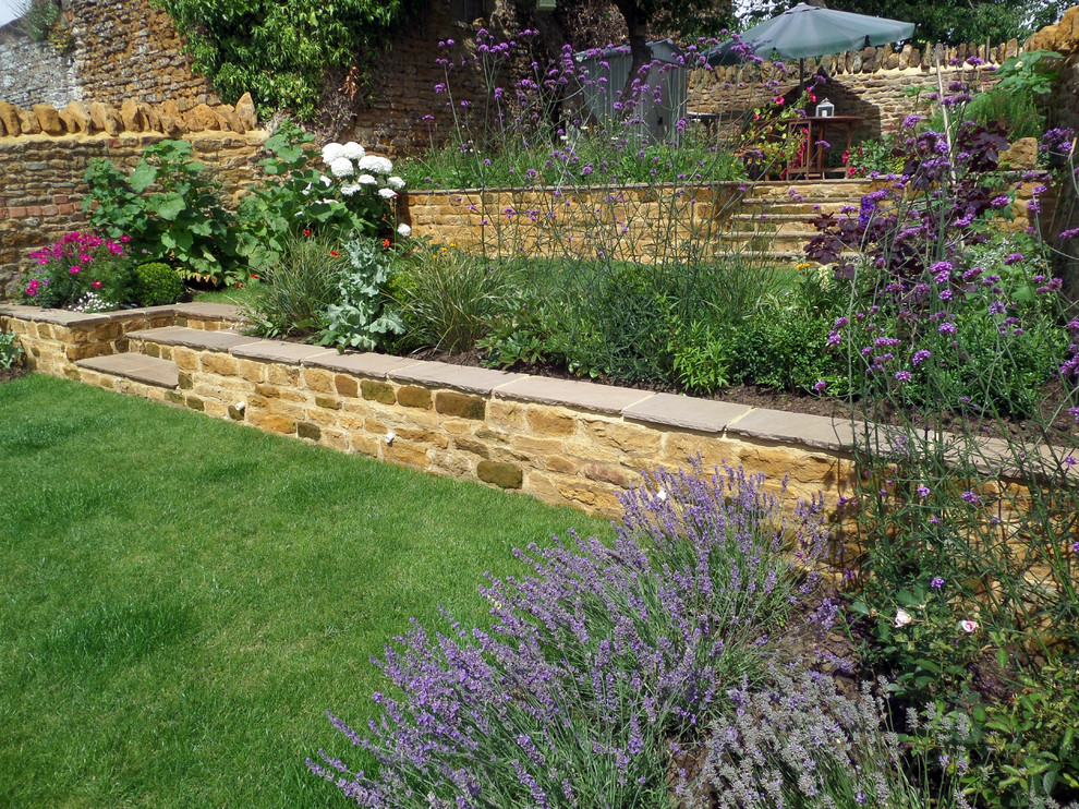 Photo of a mid-sized traditional sloped full sun garden for summer in Hertfordshire with a retaining wall and natural stone pavers.