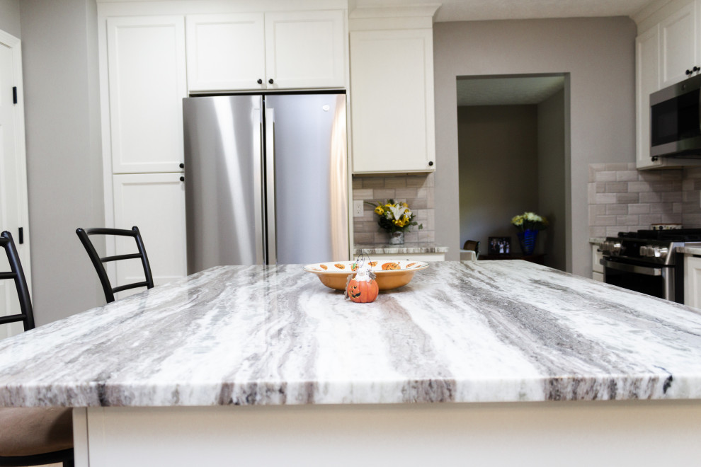 Inspiration for a transitional l-shaped light wood floor and beige floor kitchen remodel in Columbus with an undermount sink, white cabinets, gray backsplash, an island and gray countertops