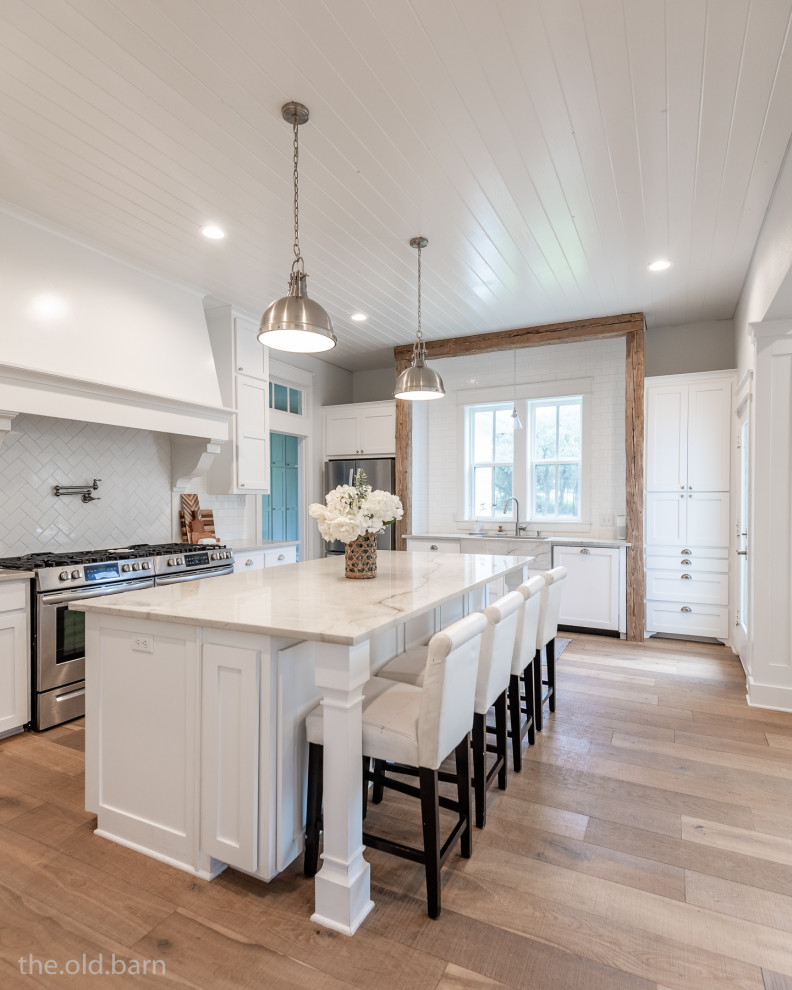 Photo of a country u-shaped open plan kitchen in Dallas with an undermount sink, shaker cabinets, white cabinets, quartzite benchtops, white splashback, subway tile splashback, stainless steel appliances, light hardwood floors, with island, brown floor, white benchtop and timber.