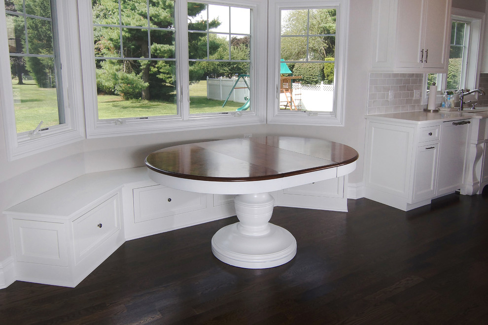 Inspiration for a large transitional u-shaped dark wood floor eat-in kitchen remodel in New York with white cabinets, white backsplash, an island, a farmhouse sink, beaded inset cabinets, subway tile backsplash and paneled appliances