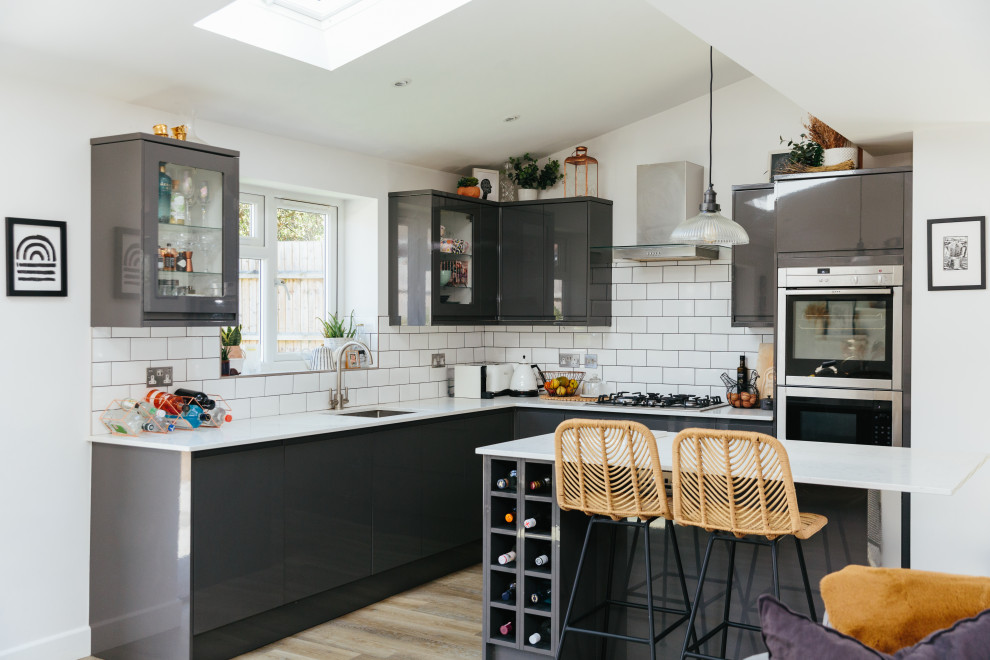 Design ideas for a medium sized contemporary open plan kitchen in London with a built-in sink, black cabinets, white splashback, stainless steel appliances, light hardwood flooring, an island, beige floors and white worktops.