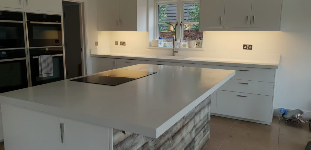 This is an example of a contemporary kitchen in Oxfordshire with concrete benchtops, panelled appliances and white benchtop.