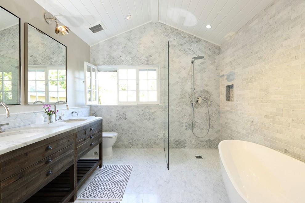 Photo of a transitional bathroom in Los Angeles with an undermount sink, dark wood cabinets, a freestanding tub, a curbless shower, a two-piece toilet and flat-panel cabinets.