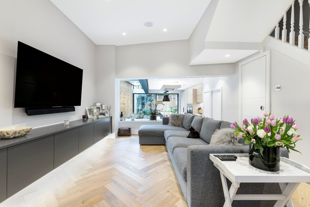 Inspiration for a mid-sized contemporary open concept living room in London with light hardwood floors, no fireplace, a wall-mounted tv, beige floor and white walls.