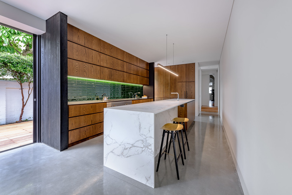 Photo of a contemporary l-shaped kitchen in Sydney with an undermount sink, flat-panel cabinets, medium wood cabinets, green splashback, stainless steel appliances, concrete floors, with island, grey floor and white benchtop.