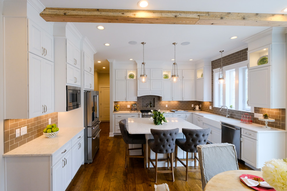 Eat-in kitchen - large transitional u-shaped dark wood floor and brown floor eat-in kitchen idea with a farmhouse sink, raised-panel cabinets, white cabinets, quartz countertops, brown backsplash, stainless steel appliances and an island