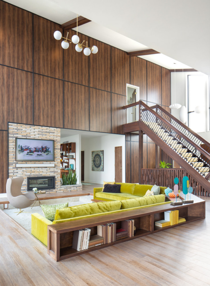 Mid-sized midcentury open concept living room in Detroit with a library, white walls, medium hardwood floors, a two-sided fireplace, a brick fireplace surround, brown floor and wallpaper.