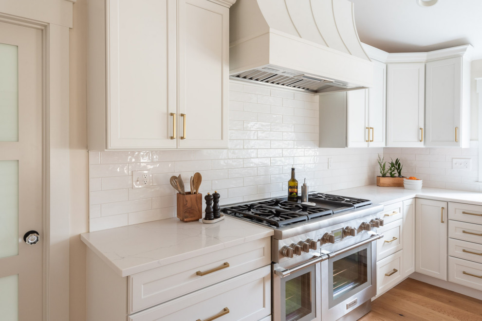 Inspiration for a huge transitional l-shaped light wood floor, brown floor and vaulted ceiling eat-in kitchen remodel in Boston with an undermount sink, shaker cabinets, white cabinets, quartz countertops, white backsplash, ceramic backsplash, paneled appliances, an island and white countertops