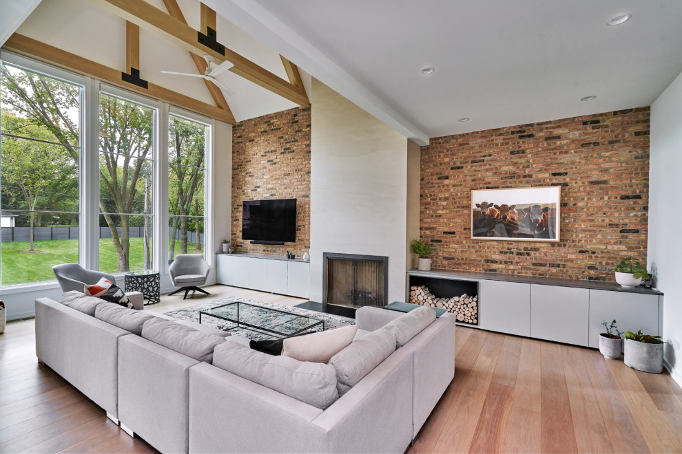 Large modern open concept living room in Chicago with white walls, light hardwood floors, a standard fireplace, a tile fireplace surround, a wall-mounted tv, exposed beam and brick walls.