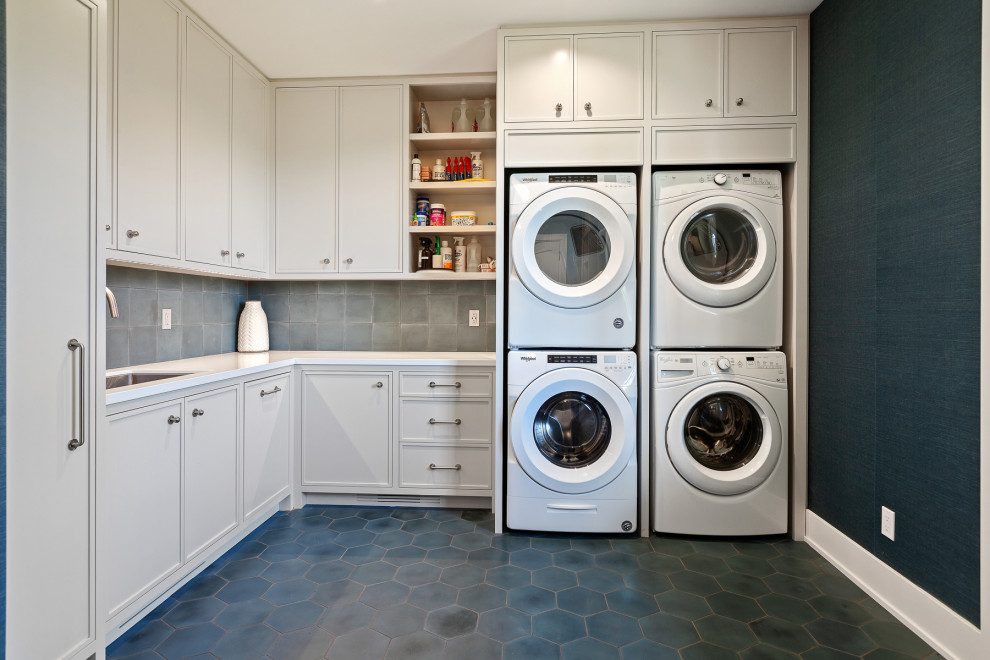 Inspiration for a transitional l-shaped laundry room in Seattle with an undermount sink, recessed-panel cabinets, grey cabinets, blue walls, a stacked washer and dryer, blue floor, white benchtop and wallpaper.