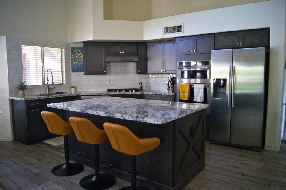 Open concept kitchen - mid-sized modern l-shaped porcelain tile and gray floor open concept kitchen idea in Phoenix with an undermount sink, shaker cabinets, brown cabinets, granite countertops, white backsplash, subway tile backsplash, stainless steel appliances, an island and white countertops