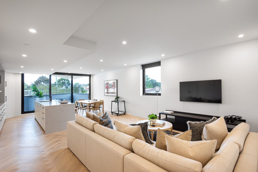 Inspiration for a contemporary open concept living room in Melbourne with white walls, light hardwood floors, a wall-mounted tv and beige floor.