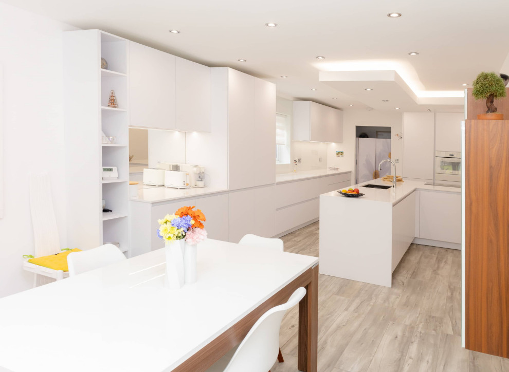 Design ideas for a small modern eat-in kitchen in Manchester with a single-bowl sink, flat-panel cabinets, white splashback, white appliances, grey floor and white benchtop.