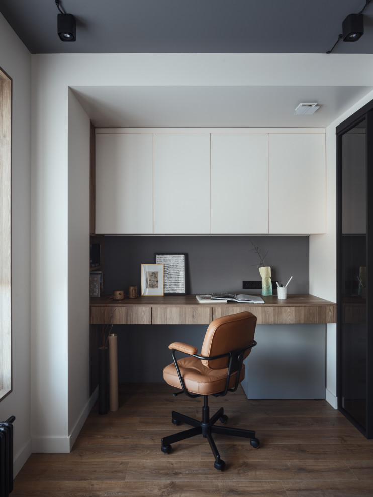 Foto de despacho industrial de tamaño medio con paredes blancas, suelo laminado, escritorio empotrado, suelo marrón y bandeja