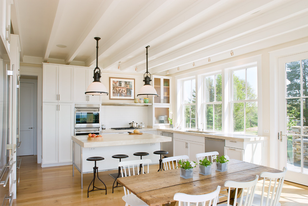 Country l-shaped eat-in kitchen in Providence with an undermount sink, shaker cabinets, white cabinets, white splashback, stainless steel appliances, medium hardwood floors and with island.