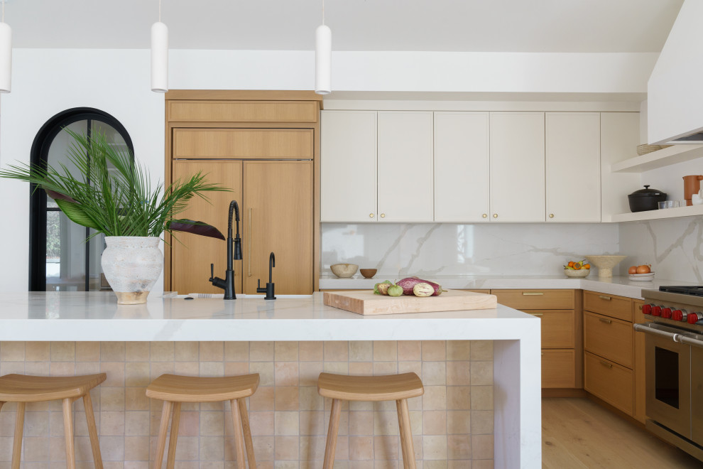 Photo of a large beach style l-shaped open plan kitchen in San Diego with an undermount sink, shaker cabinets, light wood cabinets, quartz benchtops, white splashback, engineered quartz splashback, panelled appliances, light hardwood floors, with island, beige floor, white benchtop and vaulted.