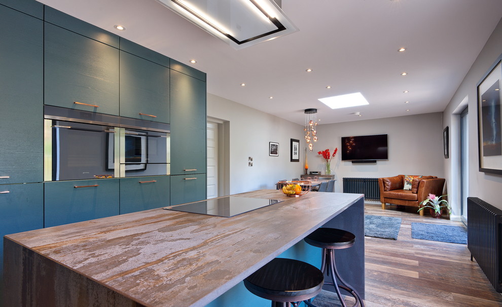Design ideas for a mid-sized contemporary l-shaped open plan kitchen in Other with a drop-in sink, flat-panel cabinets, green cabinets, tile benchtops, grey splashback, timber splashback, stainless steel appliances, laminate floors, with island, brown floor and brown benchtop.