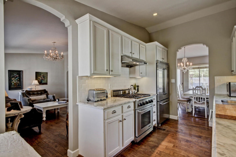 Mid-sized traditional galley eat-in kitchen in Phoenix with an undermount sink, shaker cabinets, white cabinets, marble benchtops, white splashback, subway tile splashback, stainless steel appliances and medium hardwood floors.