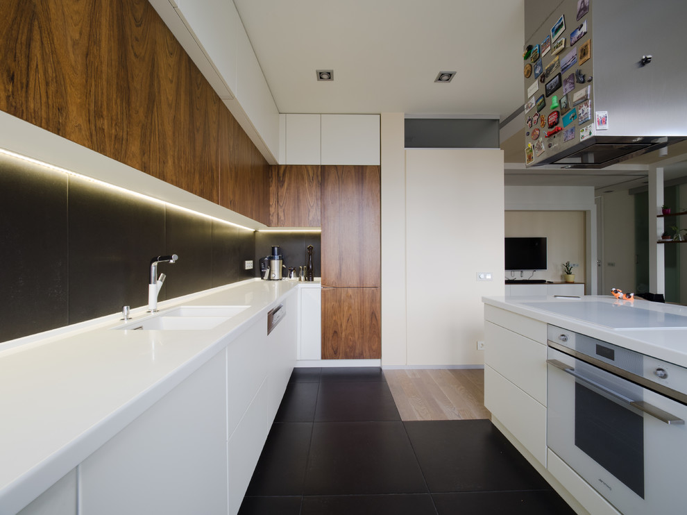 Design ideas for a large contemporary l-shaped open plan kitchen in Moscow with an undermount sink, flat-panel cabinets, white cabinets, solid surface benchtops, black splashback, porcelain splashback, white appliances, ceramic floors, with island and black floor.