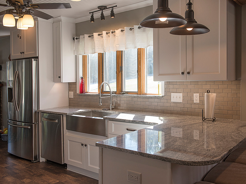 Example of a small mountain style l-shaped dark wood floor eat-in kitchen design with a farmhouse sink, shaker cabinets, white cabinets, granite countertops, beige backsplash, ceramic backsplash, stainless steel appliances and a peninsula