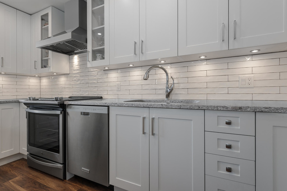 Mid-sized arts and crafts l-shaped eat-in kitchen in Vancouver with an undermount sink, raised-panel cabinets, white cabinets, quartz benchtops, white splashback, ceramic splashback, stainless steel appliances, laminate floors, with island, brown floor and grey benchtop.