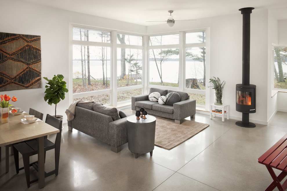This is an example of a contemporary open concept family room in Portland Maine with concrete floors, grey walls, a wood stove and grey floor.