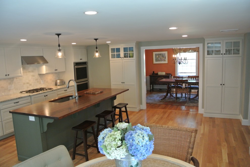 Eat-in kitchen - transitional galley light wood floor eat-in kitchen idea in Boston with an undermount sink, shaker cabinets, white cabinets, wood countertops, white backsplash, ceramic backsplash, stainless steel appliances, an island and brown countertops