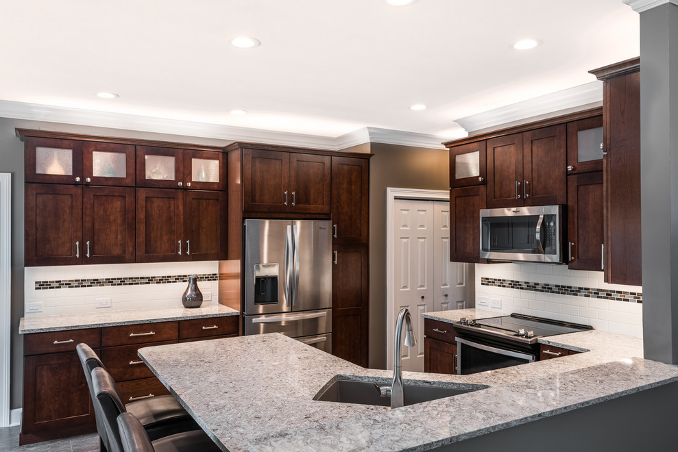 Mid-sized transitional u-shaped vinyl floor and brown floor kitchen photo with an undermount sink, recessed-panel cabinets, brown cabinets, quartz countertops, multicolored backsplash, porcelain backsplash, stainless steel appliances, a peninsula and multicolored countertops