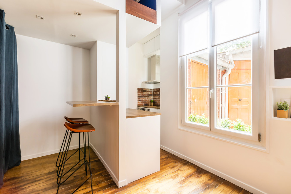 Small industrial galley eat-in kitchen in Paris with an undermount sink, beaded inset cabinets, white cabinets, wood benchtops, brown splashback, brick splashback, stainless steel appliances, medium hardwood floors, with island, brown floor and brown benchtop.