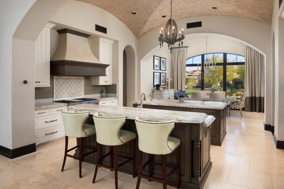 This is an example of an expansive mediterranean u-shaped open plan kitchen in Phoenix with a farmhouse sink, raised-panel cabinets, brown cabinets, quartzite benchtops, multi-coloured splashback, porcelain splashback, stainless steel appliances, porcelain floors, multiple islands, beige floor and multi-coloured benchtop.