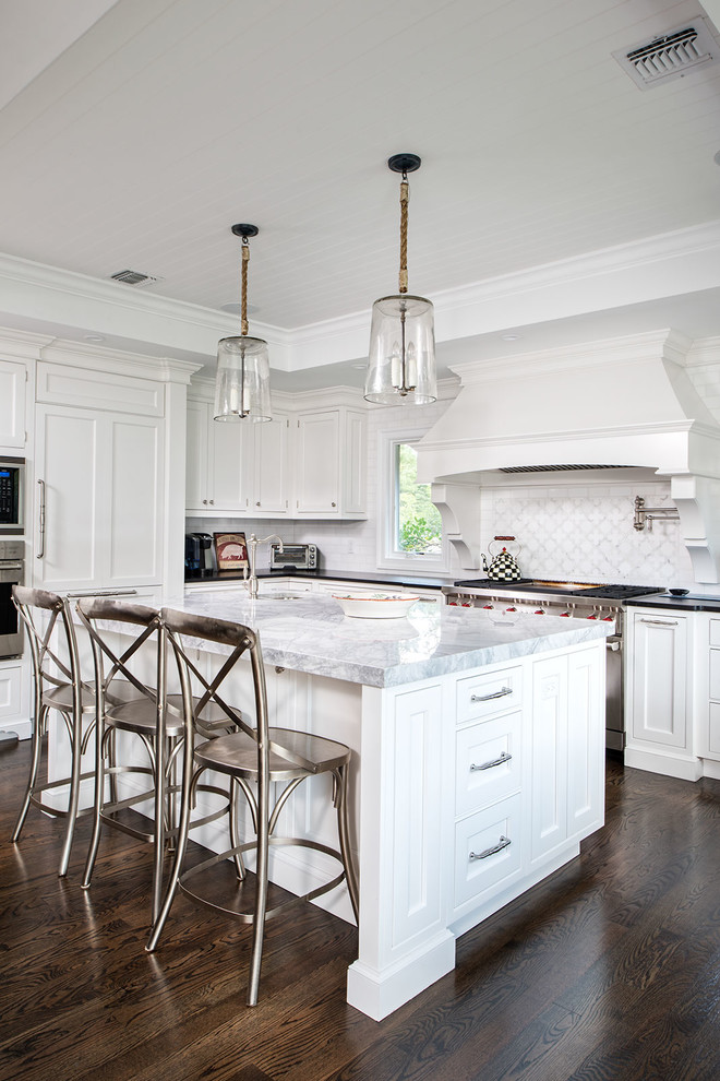 This is an example of a large traditional l-shaped kitchen in New York with white cabinets, quartzite benchtops, panelled appliances, dark hardwood floors, with island, white splashback and beaded inset cabinets.