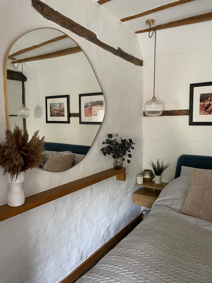 Ejemplo de dormitorio principal actual pequeño con paredes beige, suelo de madera oscura, todas las chimeneas, marco de chimenea de ladrillo, suelo marrón, vigas vistas y ladrillo