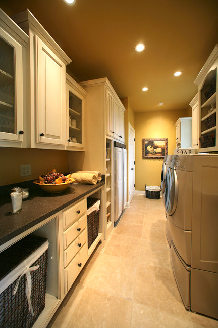 This is an example of a large transitional galley utility room in Other with raised-panel cabinets, white cabinets, solid surface benchtops, travertine floors, a side-by-side washer and dryer and brown walls.