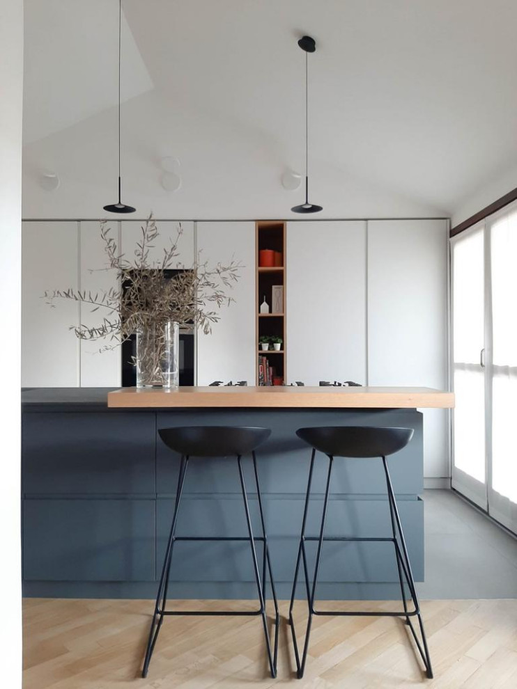 Mid-sized modern galley open plan kitchen in Milan with a drop-in sink, beaded inset cabinets, grey cabinets, limestone benchtops, black splashback, black appliances, ceramic floors, with island, grey floor and black benchtop.