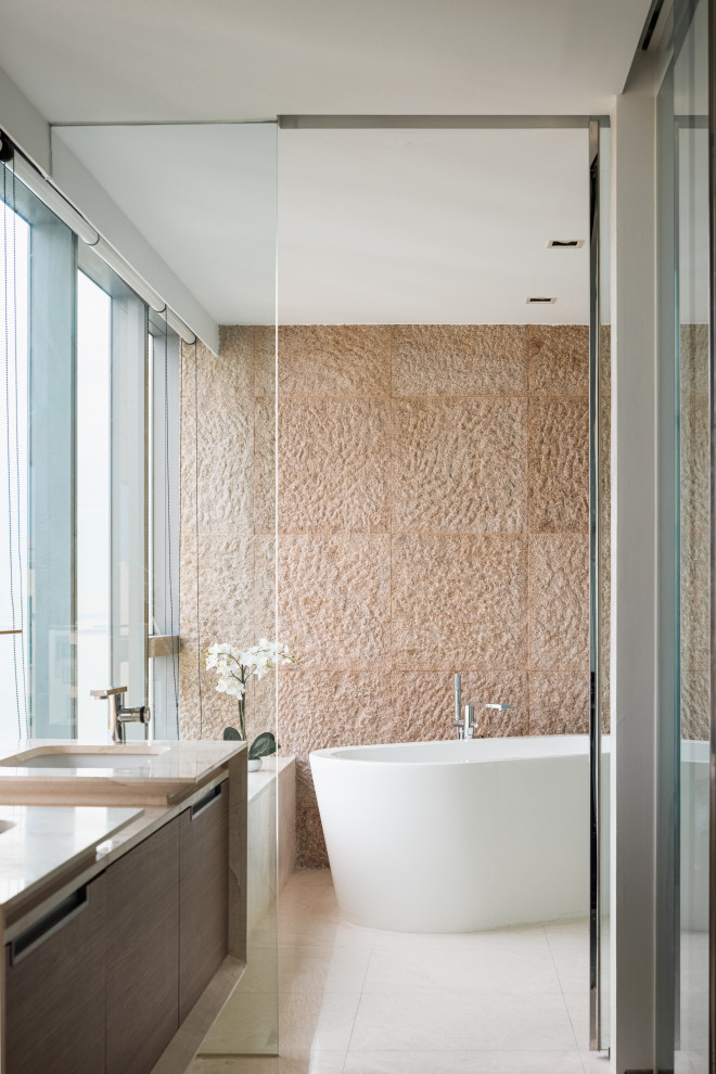 Cette photo montre une salle de bain tendance en bois brun avec un placard à porte plane, une baignoire indépendante, un carrelage beige, un mur beige, un lavabo encastré, un sol beige, aucune cabine, un plan de toilette beige, meuble double vasque et meuble-lavabo suspendu.