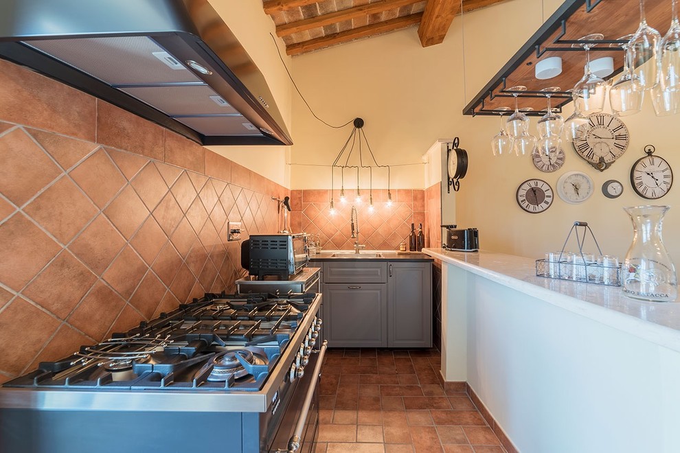 Inspiration for a small country l-shaped eat-in kitchen in Rome with an integrated sink, raised-panel cabinets, grey cabinets, laminate benchtops, brown splashback, terra-cotta splashback, stainless steel appliances and brown floor.