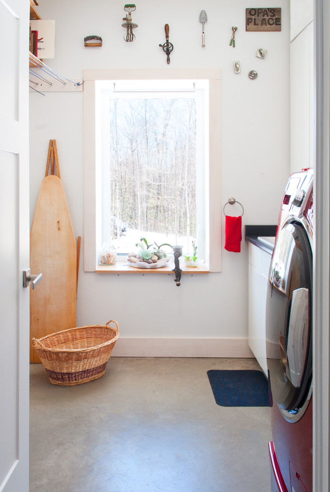 Design ideas for a mid-sized eclectic galley dedicated laundry room in Toronto with flat-panel cabinets, white cabinets, white walls and concrete floors.