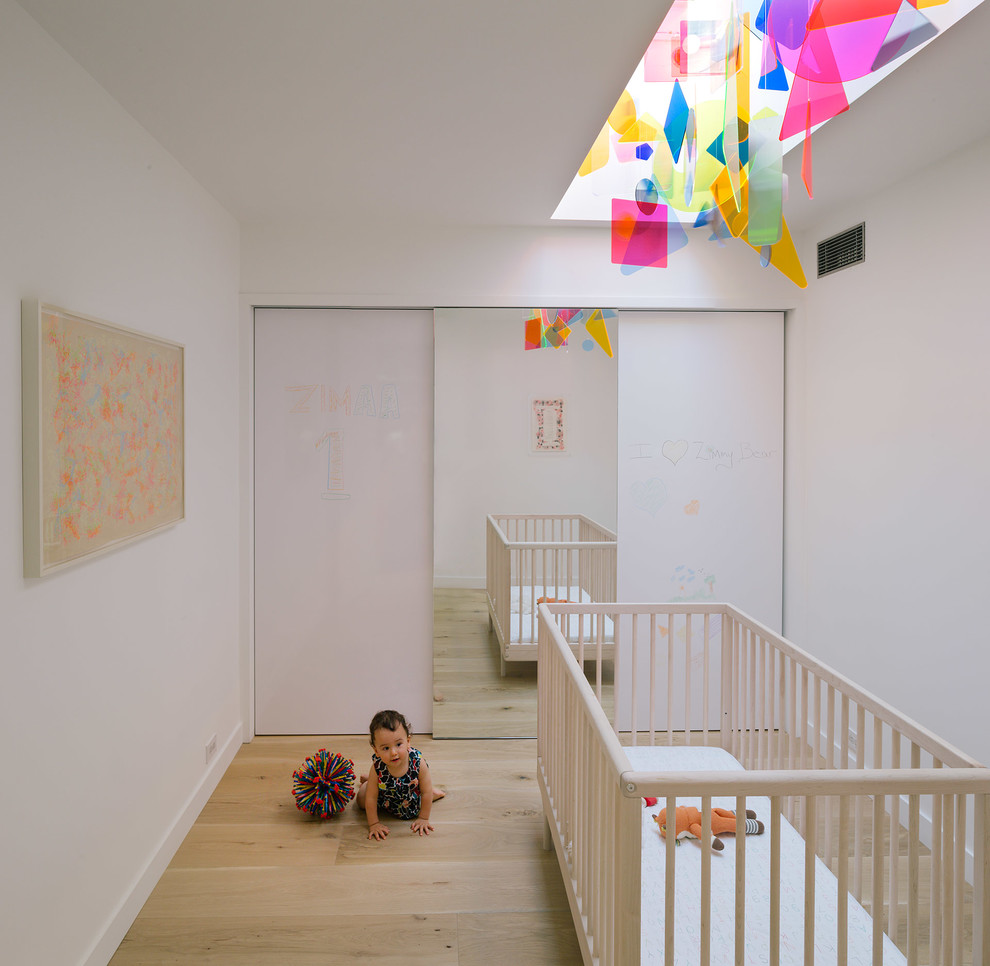 Contemporary gender-neutral nursery in New York with white walls, light hardwood floors and beige floor.