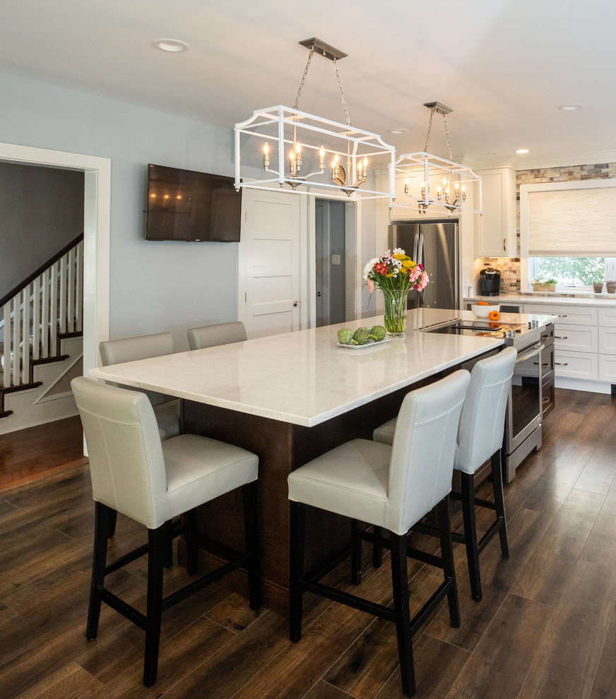 This is an example of a large transitional l-shaped open plan kitchen in Philadelphia with shaker cabinets, white cabinets, quartzite benchtops, multi-coloured splashback, glass tile splashback, stainless steel appliances, laminate floors, with island, brown floor and white benchtop.