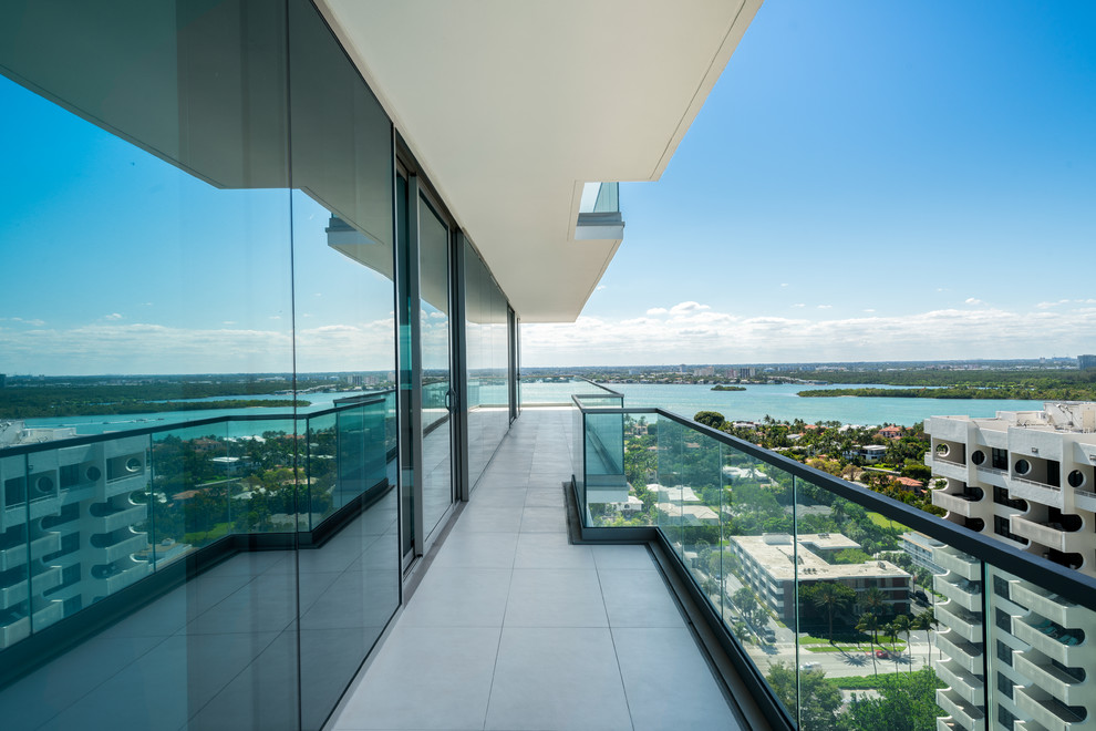 Photo of a mid-sized modern balcony in Miami with a roof extension and glass railing.