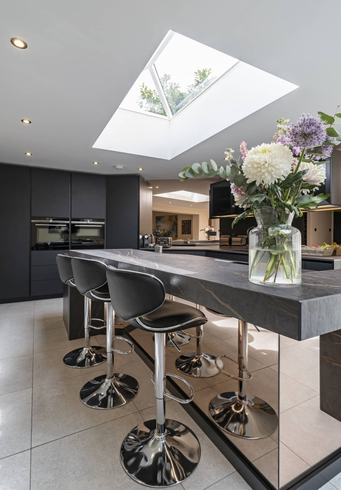 Mittelgroße Moderne Wohnküche mit integriertem Waschbecken, Glasfronten, schwarzen Schränken, Quarzit-Arbeitsplatte, Glasrückwand, schwarzen Elektrogeräten, Keramikboden, Kücheninsel, grauem Boden, bunter Arbeitsplatte und Kassettendecke in Oxfordshire