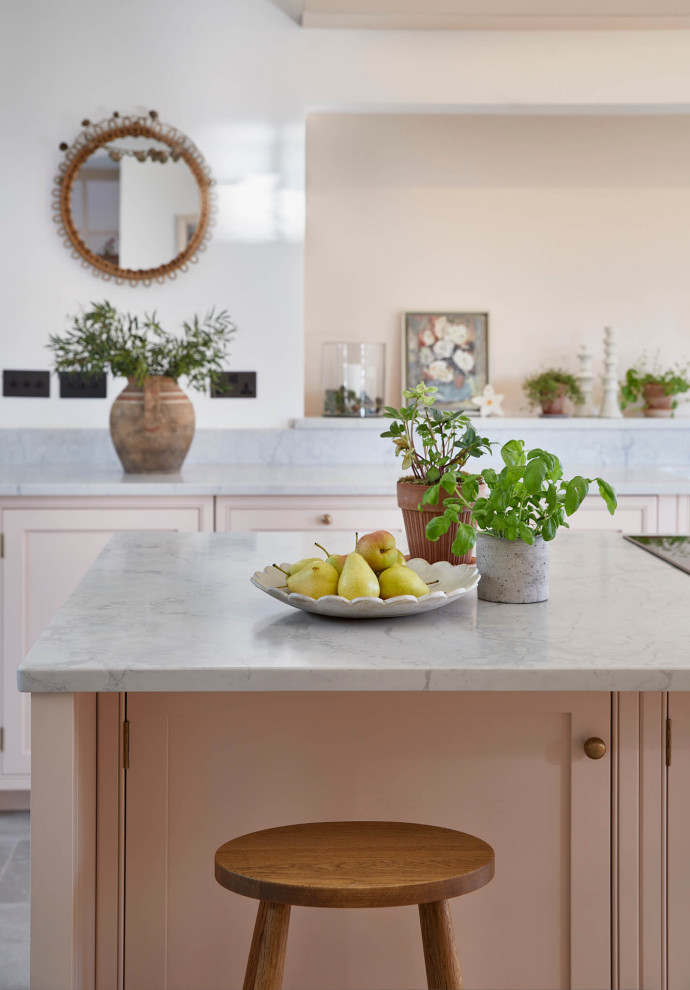 This is an example of a large rural grey and pink single-wall open plan kitchen in London with a belfast sink, shaker cabinets, pink cabinets, quartz worktops, pink splashback, black appliances, ceramic flooring, an island, multi-coloured floors, grey worktops and a vaulted ceiling.