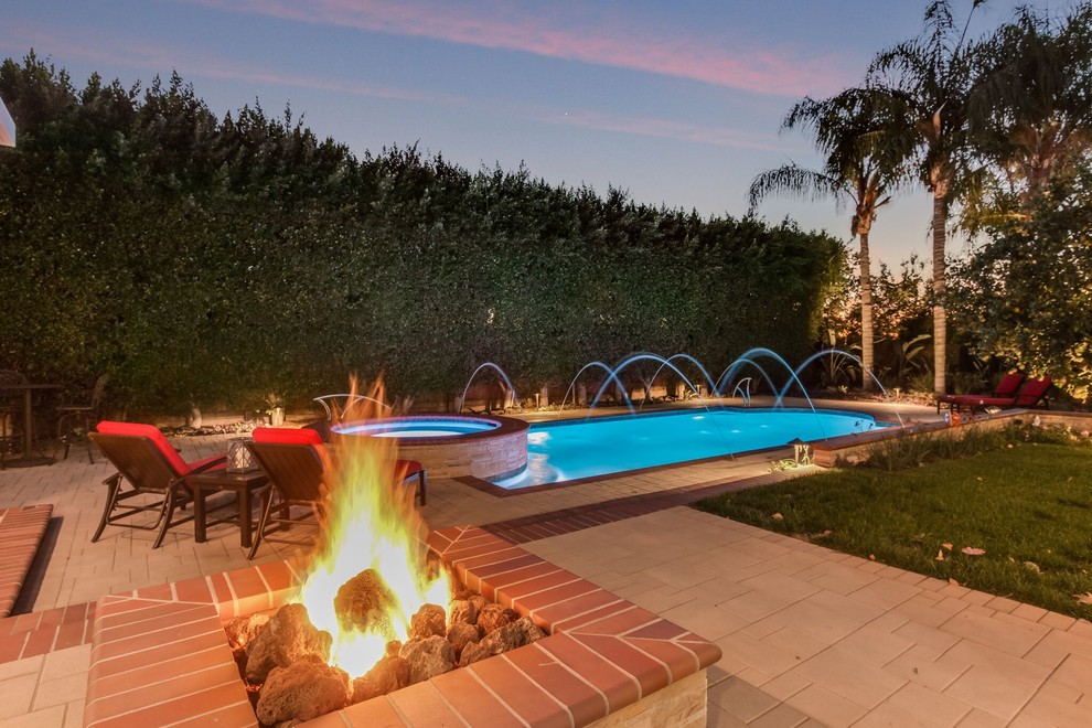 Mid-sized transitional backyard custom-shaped pool in Orange County with a hot tub and brick pavers.
