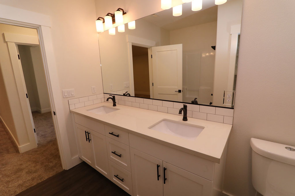 Photo of a mid-sized country kids bathroom in Portland with shaker cabinets, white cabinets, an alcove tub, an alcove shower, a one-piece toilet, gray tile, subway tile, grey walls, laminate floors, an undermount sink, engineered quartz benchtops, brown floor, a shower curtain and white benchtops.