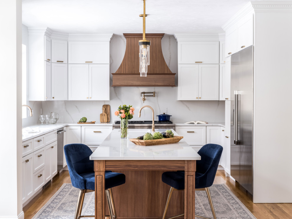 Exempel på ett klassiskt vit vitt u-kök, med en undermonterad diskho, luckor med infälld panel, vita skåp, bänkskiva i kvarts, vitt stänkskydd, rostfria vitvaror, mellanmörkt trägolv, en köksö och brunt golv
