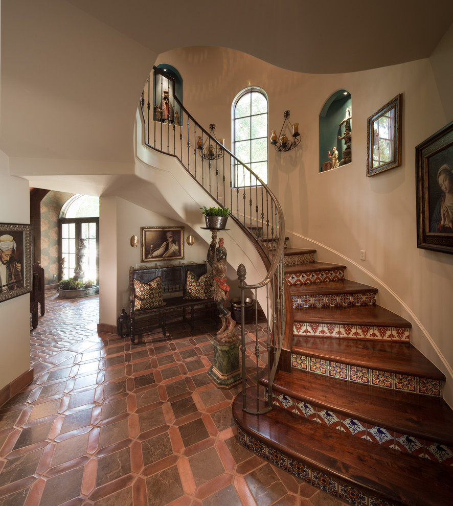 This is an example of a large mediterranean wood curved staircase in Houston with tile risers and metal railing.