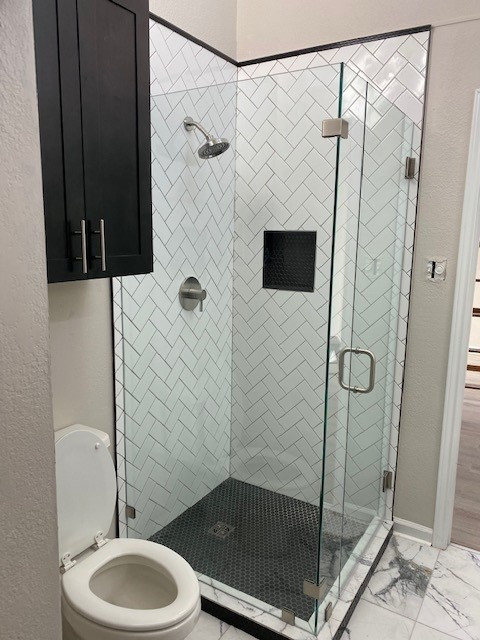 Bathroom remodel, herringbone shower subway tiles with black hexagon small tile on shower flooring.  Frameless shower doors. Black cabinets. Porcelain 24x24 tile flooring
